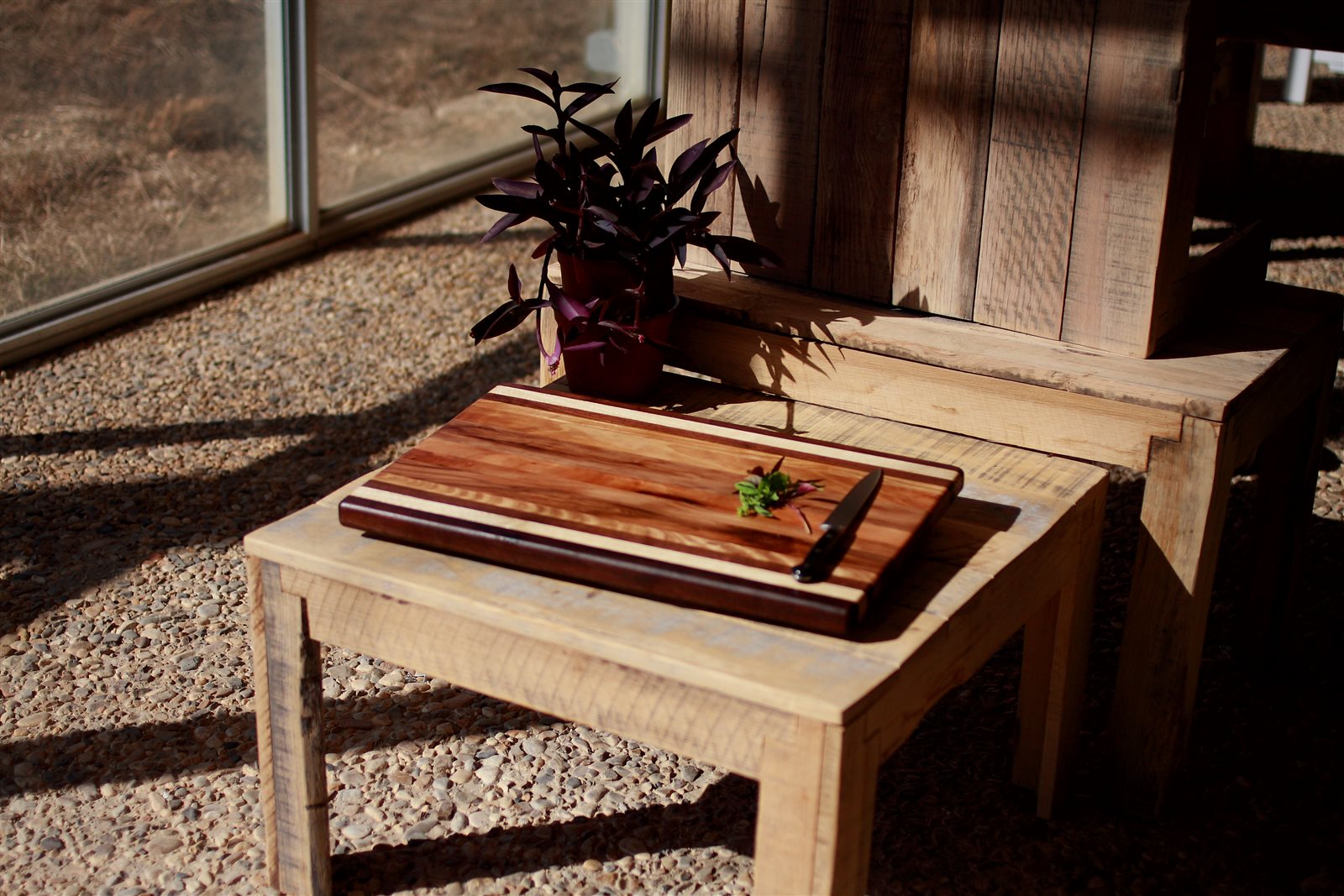 Bold Stripe meat board with alternating light and dark wood stripes, dark end caps and a juice groove, with a chef's knife and herbs on a rustic table
