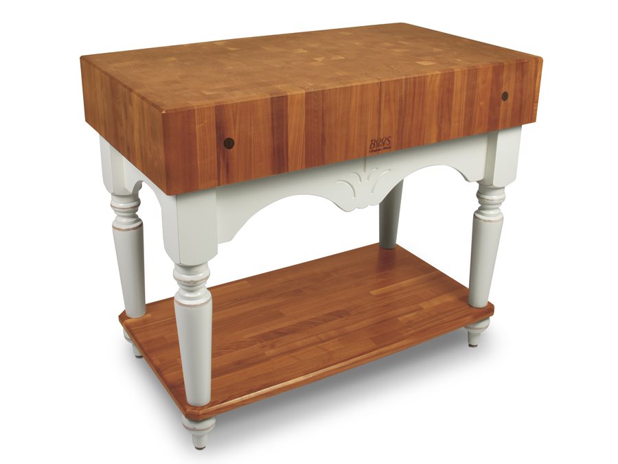 End-grain butcher block table with a cherry-toned top, cream painted base, arched apron, turned legs and a wood shelf